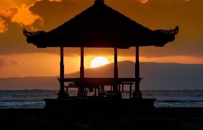 Balinese gazebo silhouette framing a golden sunrise over the ocean in Sanur